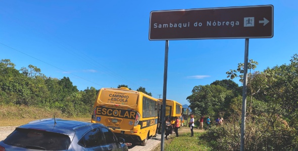 Carros estacionados com destaque para uma placa sinalizando a entrada do acesso ao Sambaqui do Nobrega