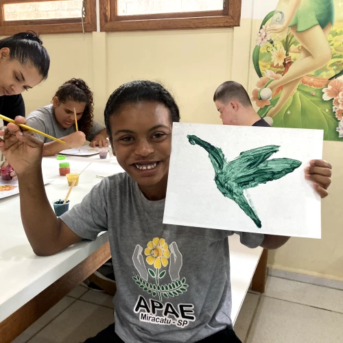 Aluna da APAE exibindo seu desenho de um pássaro