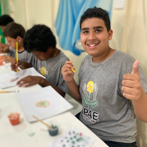 Aluno da Apae, fazendo seu desenho com os pigmentos naturais, e acenando para a câmera